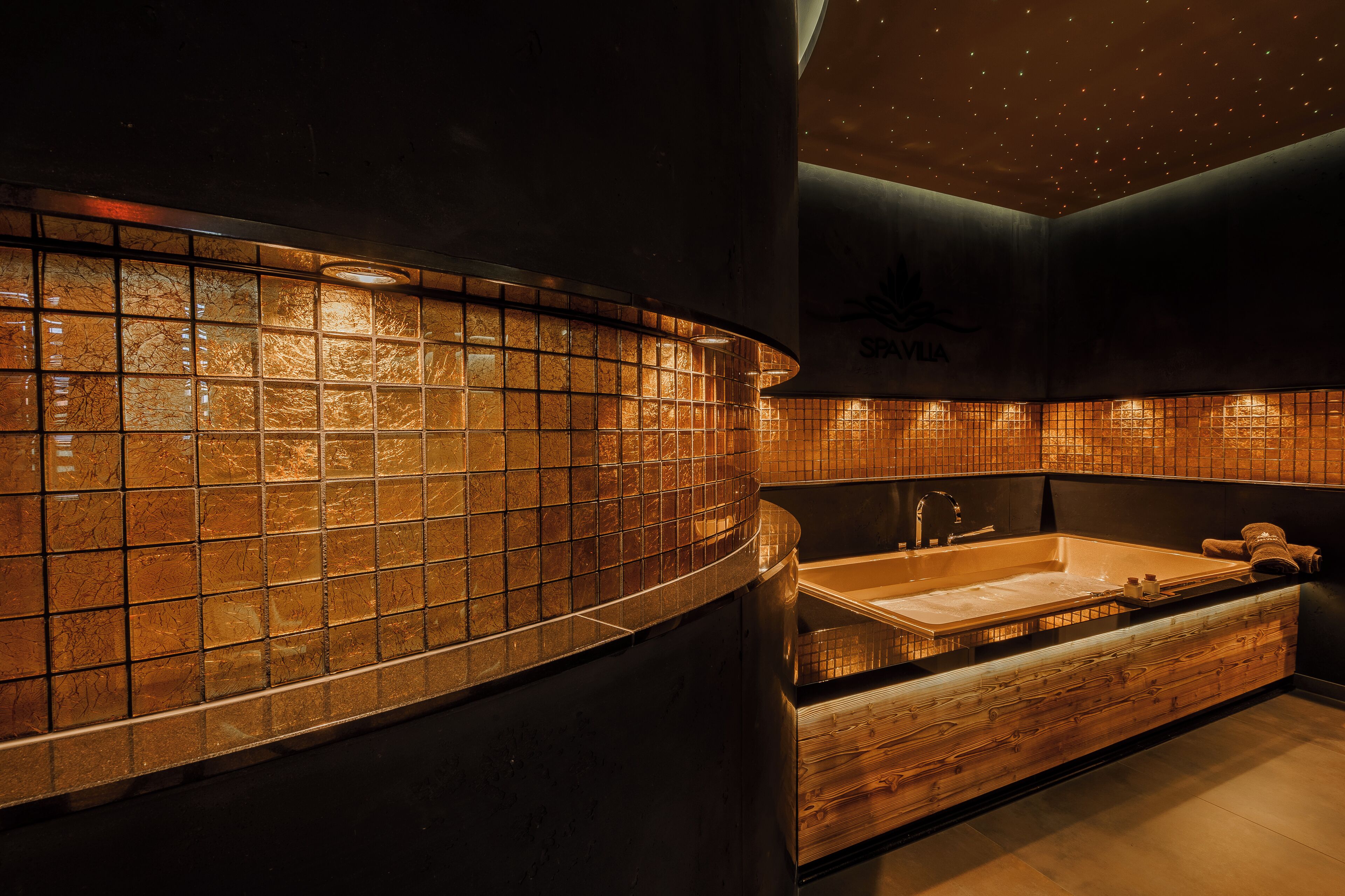 A modern bathroom with a large bathtub, a wooden vanity, and a tiled wall.