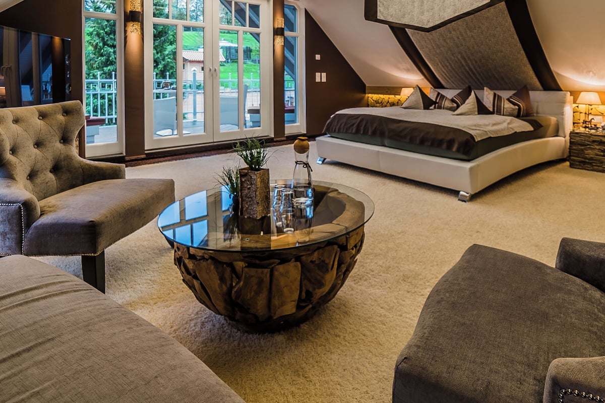 Une chambre spacieuse de style loft, avec un plafond en pente, un grand lit et une table basse en verre.