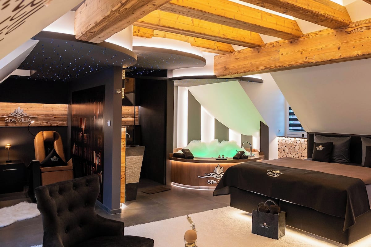Une villa de style moderne avec un espace spa, comprenant une chambre confortable, un coin salon doté d’une cheminée et un espace bien-être avec une grande baignoire.