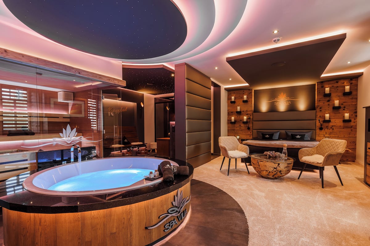 Une salle de spa moderne équipée d’un jacuzzi, d’un coin salon et d’une cheminée fixée au mur.