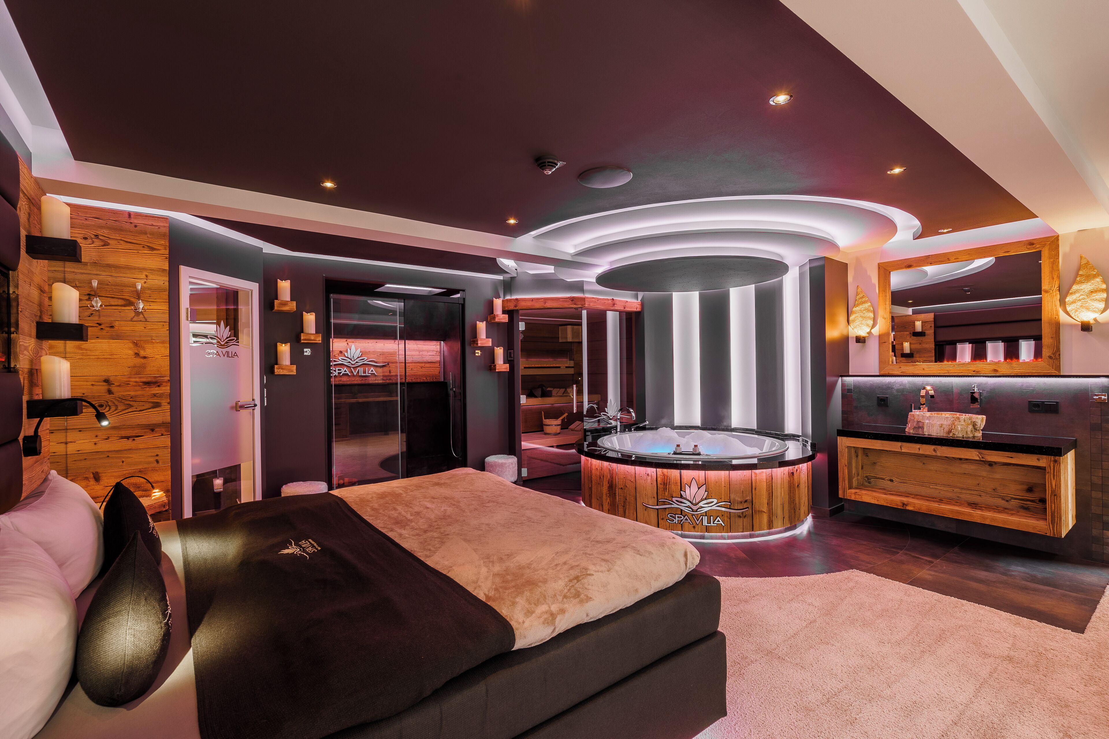 A modern spa room with a wooden wall, a massage table, a hot tub, and a vanity with a mirror.