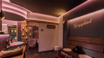 A modern spa area with a wooden bench, a stone basin, and a wall with the name 'Kneippbad'.