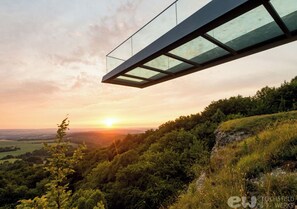 A modern glass bridge over a forested hillside at sunset. - SPA VILLA Beauty und Wellness Resort (Wingerode)