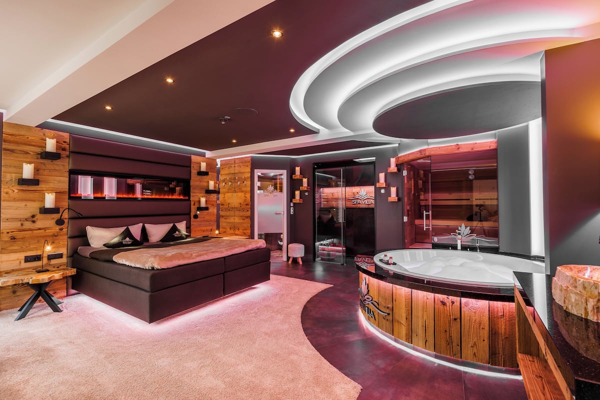 Une salle de spa moderne avec un grand lit, un comptoir d’accueil en bois et un jacuzzi.