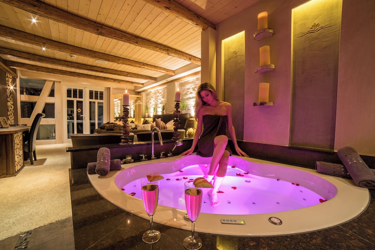 Un espace de bien-être avec un jacuzzi, des bougies et une femme assise près du jacuzzi.