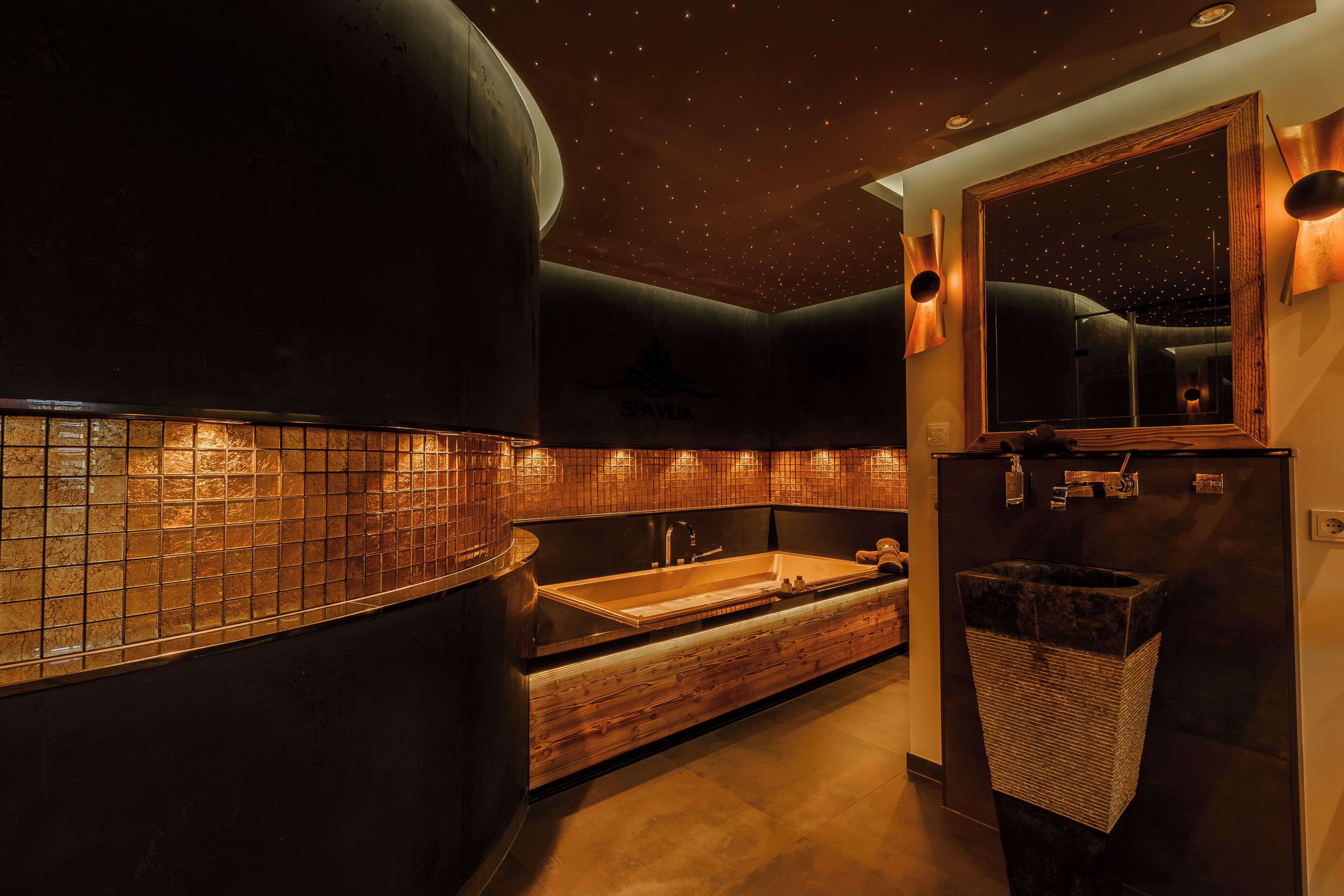 A modern bathroom with a large bathtub, a wooden vanity, and a mirror with a starry ceiling.
