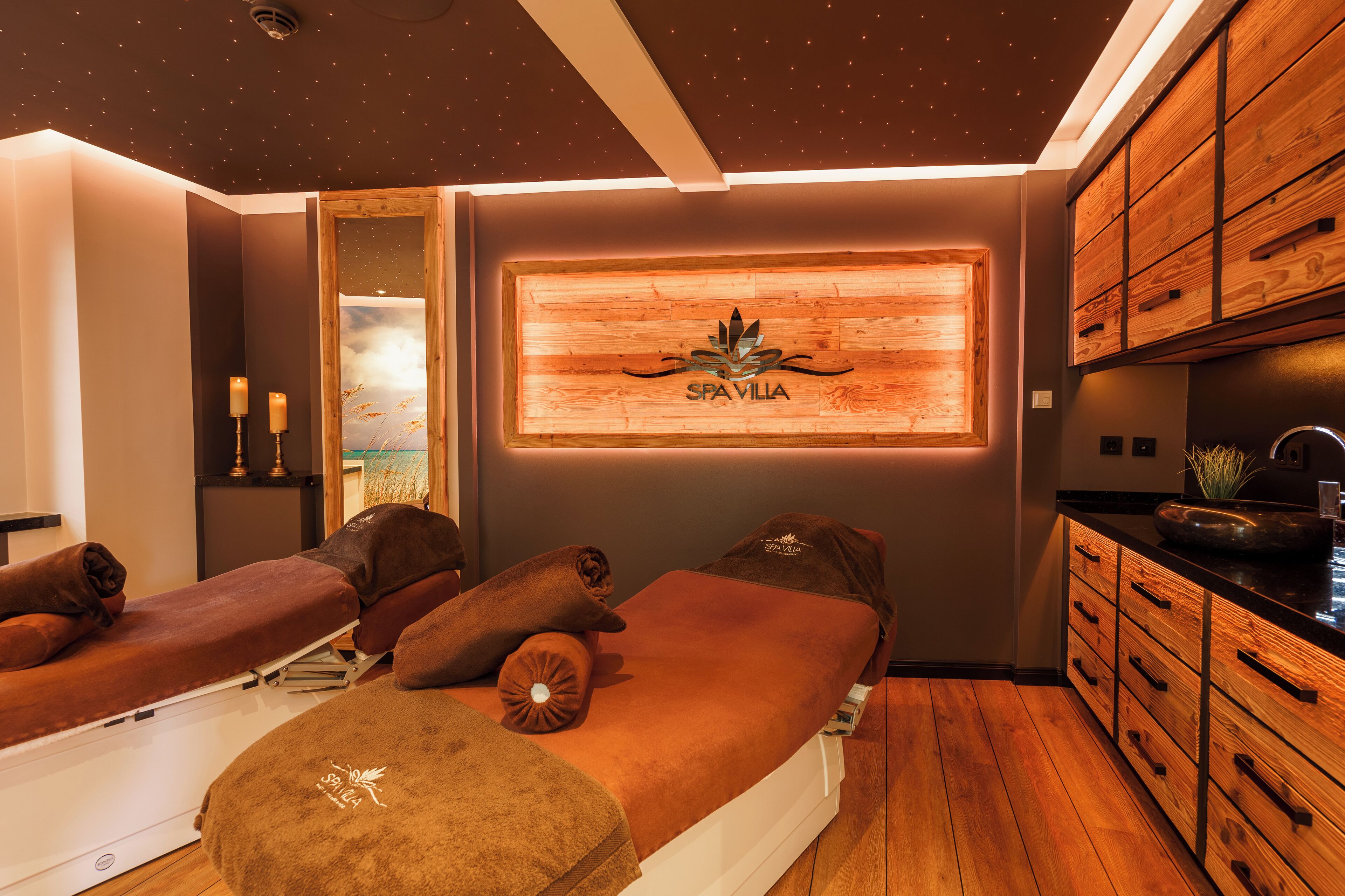A spa room with wooden paneling, a wall-mounted logo, and two massage tables with towels.