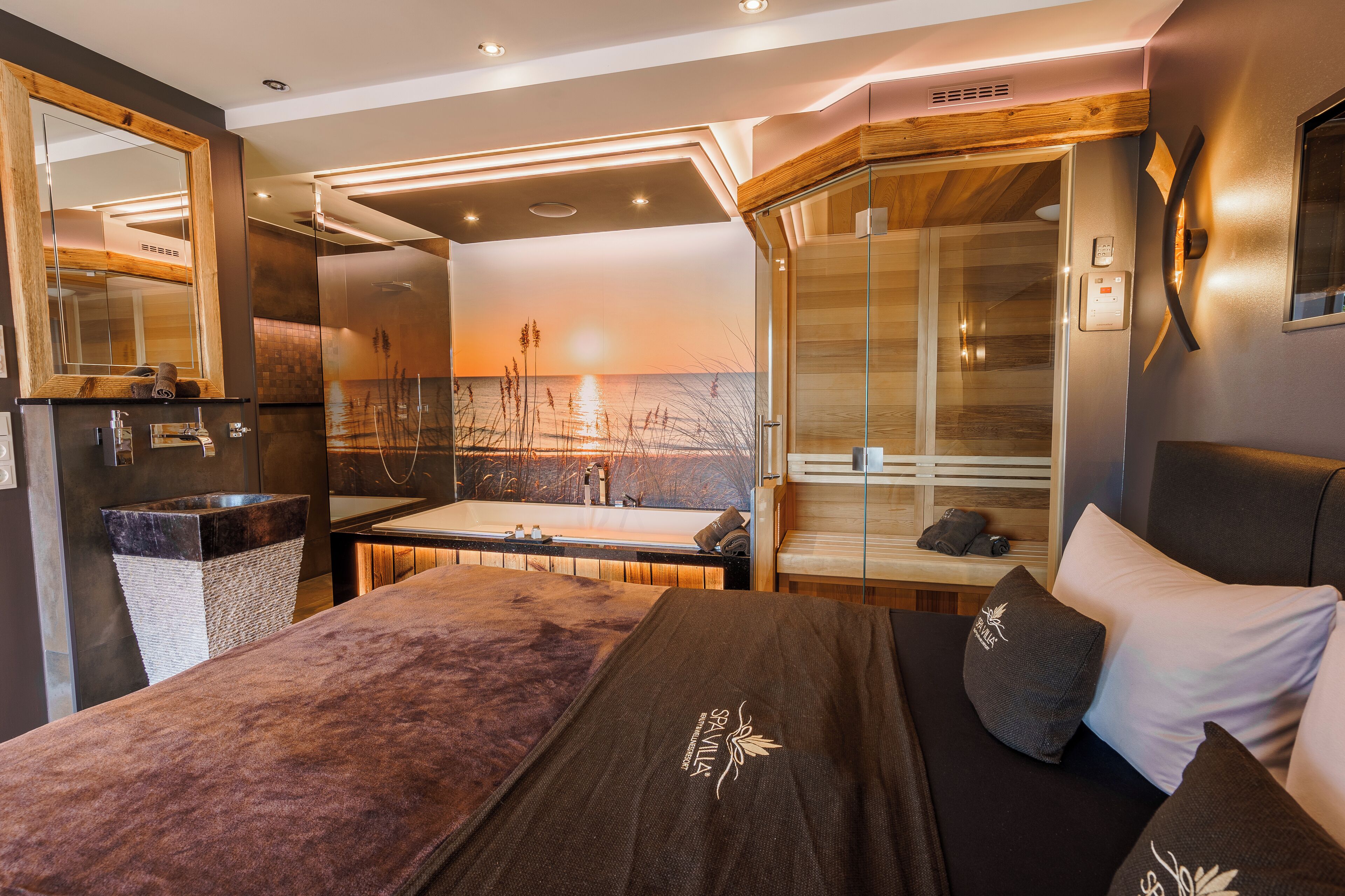 A modern spa room with a large bed, a glass shower enclosure, and a view of the sunset through the shower window.