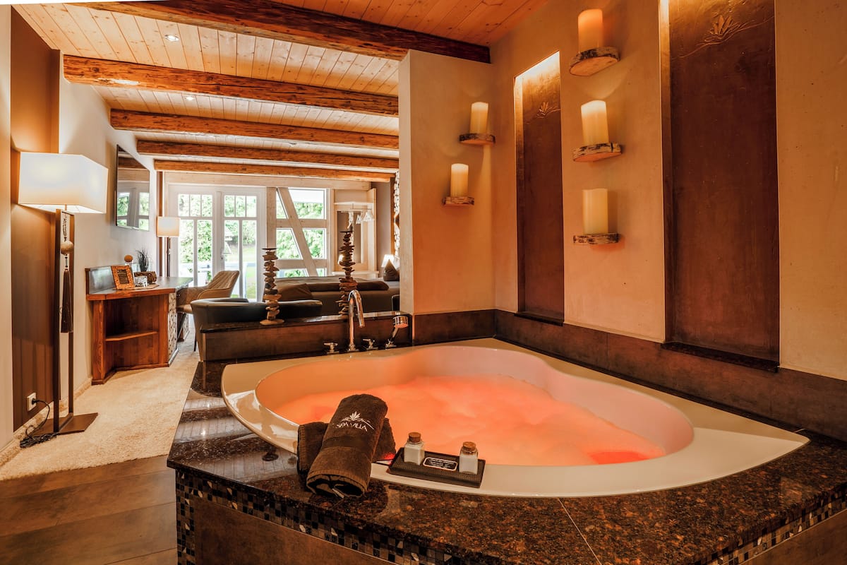 Une salle de bain spacieuse avec une grande baignoire, des poutres en bois au plafond et une vue sur l’extérieur.
