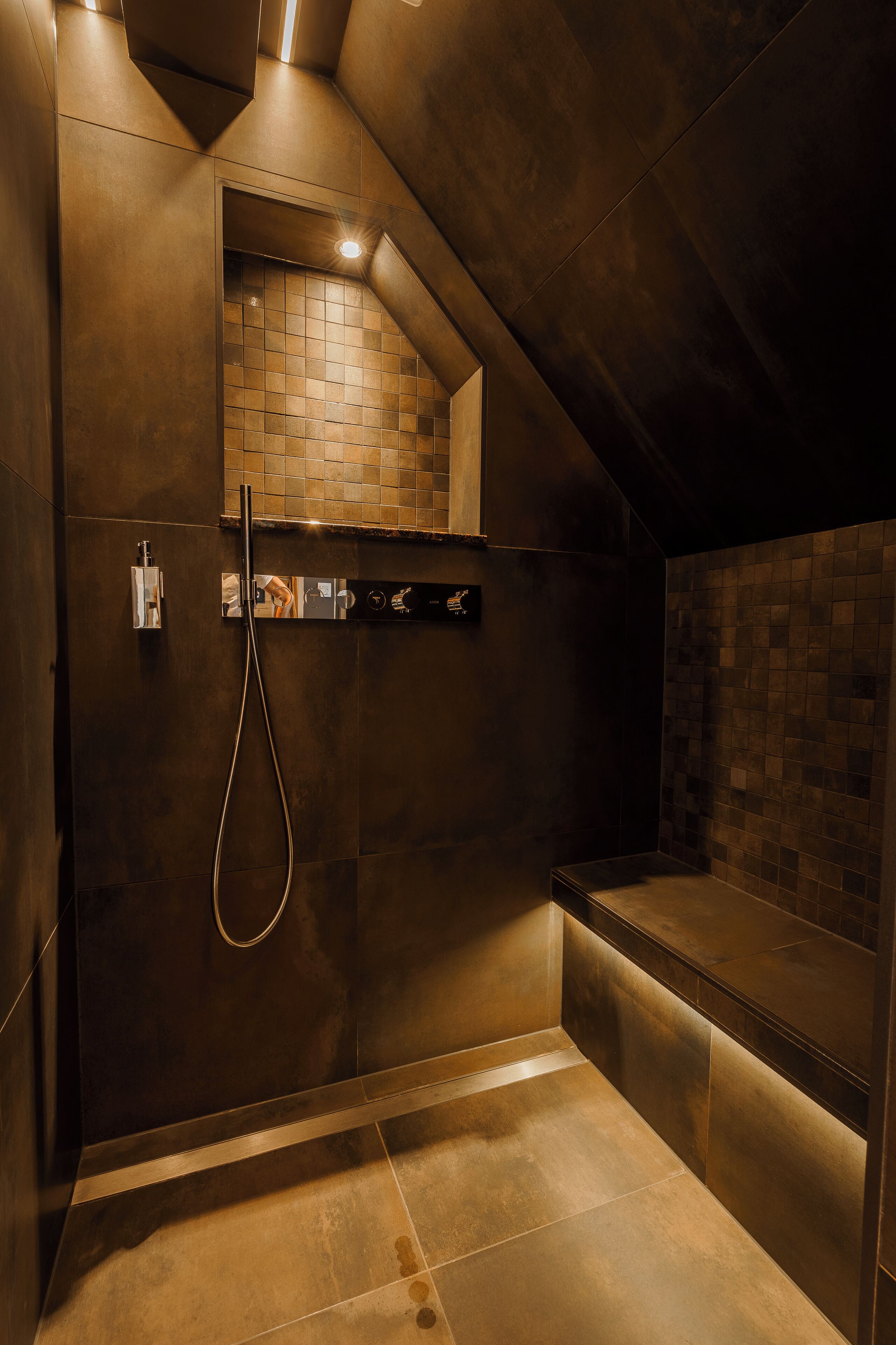 Ein modernes Duschbad mit gefliesten Wänden, einer integrierten Sitzbank und einer Handbrause.