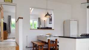 A kitchen with a wooden bench, a table with a white tablecloth, a hanging light fixture, and a refrigerator.