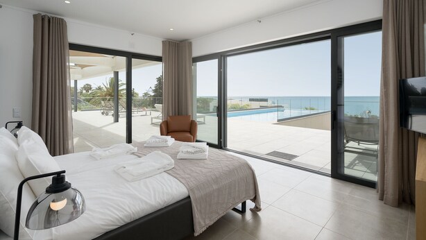 Quarto moderno com uma cama grande, televisão e vista para uma piscina e oceano.