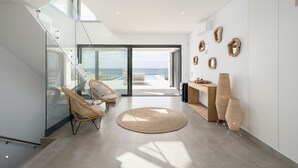 Um interior moderno com escada de vidro, cadeiras de vime, tapete redondo e vista para o oceano.