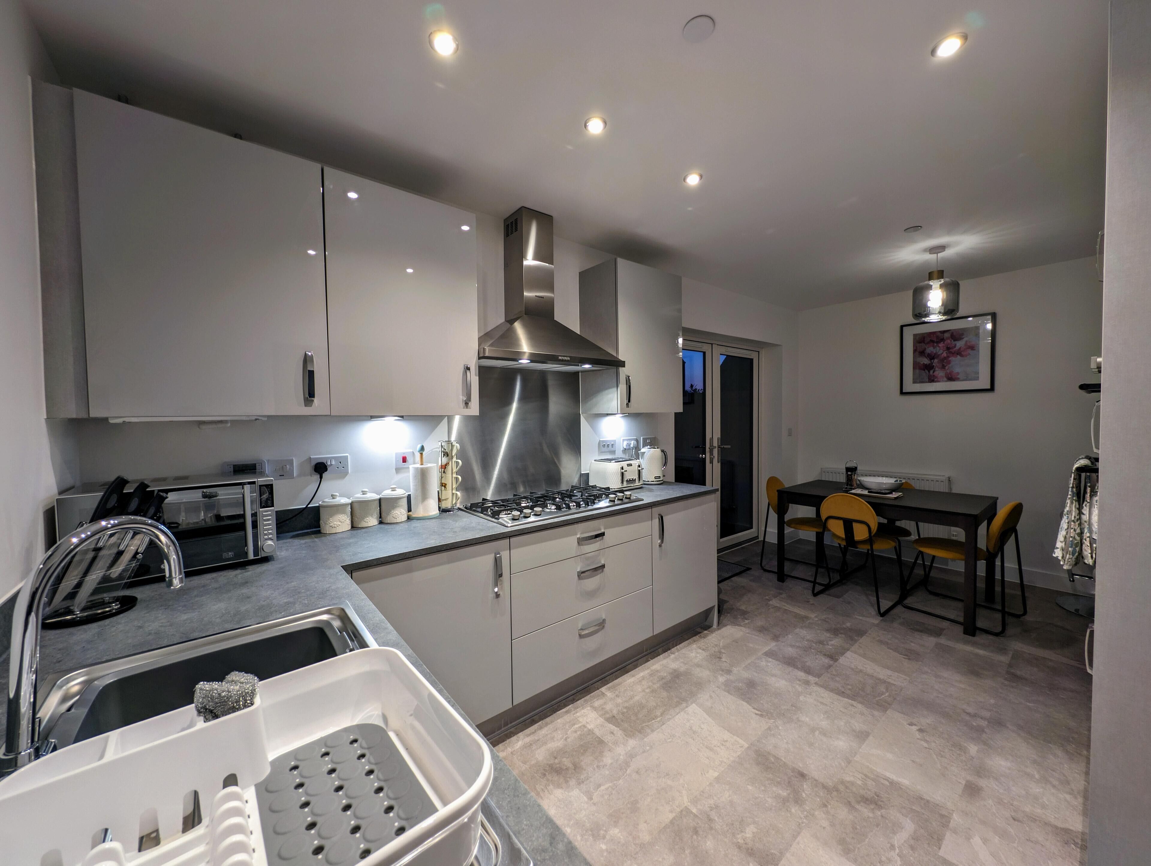 A modern kitchen with grey cabinets, a stainless steel range hood, and a dining area with a table and chairs.