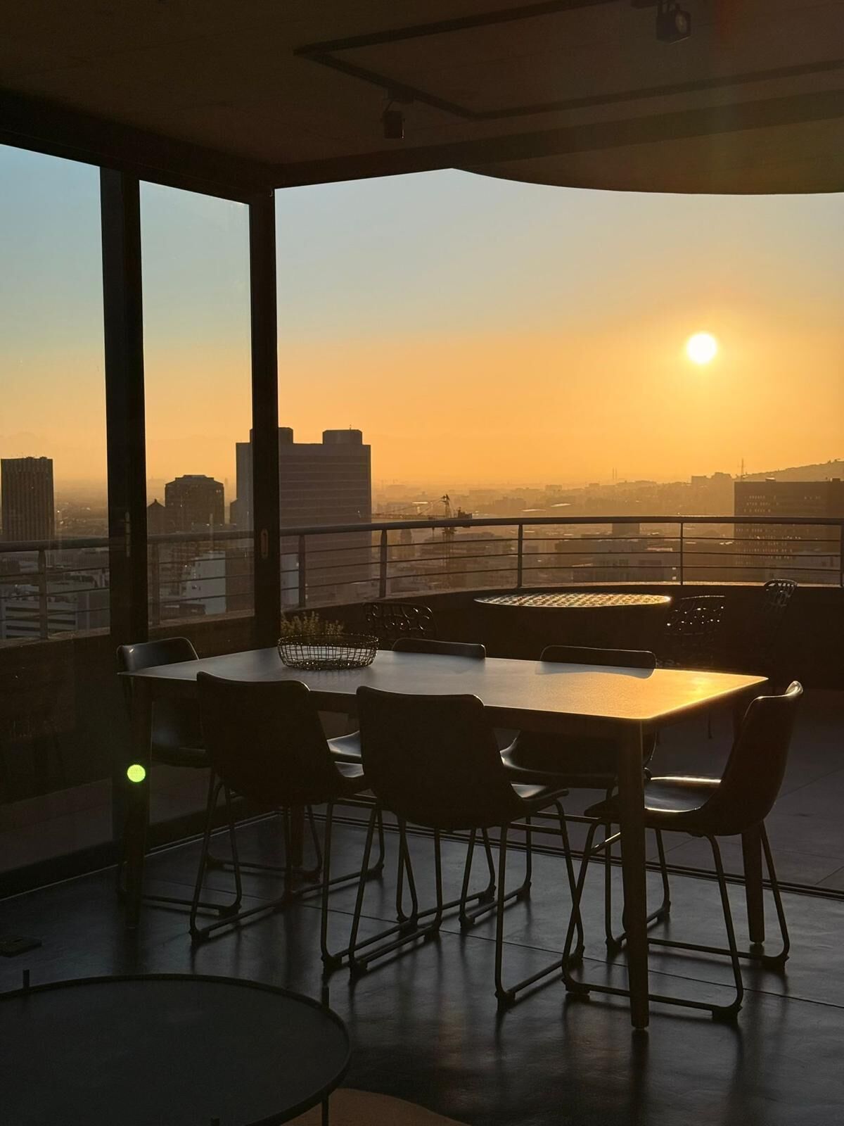 Un espace repas comprenant une table et des chaises, de grandes fenêtres et une vue sur la ville au coucher du soleil.