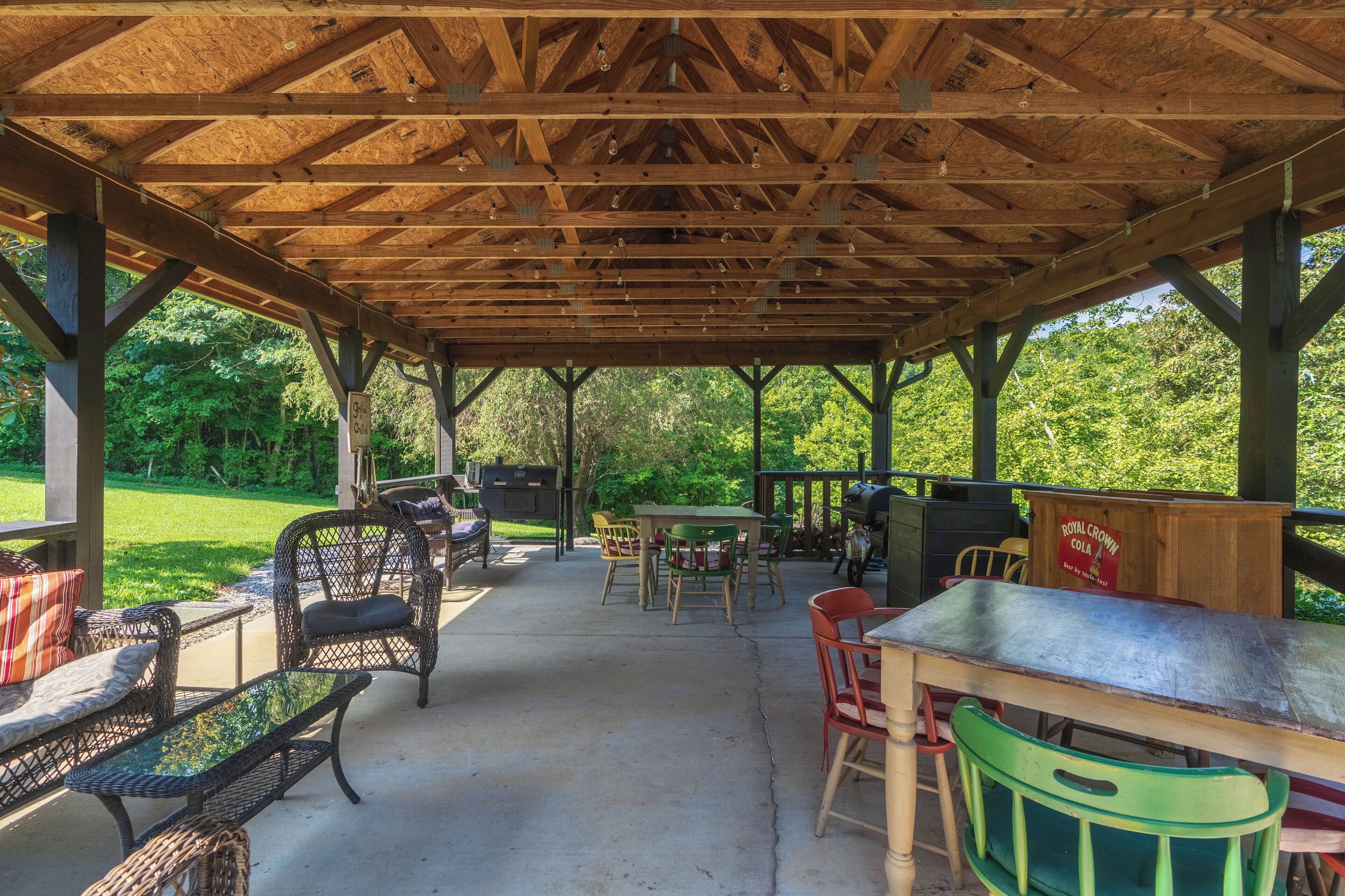 An outdoor covered patio with wooden beams, wicker furniture, and a table with a sign reading "Royal Crown Cola."