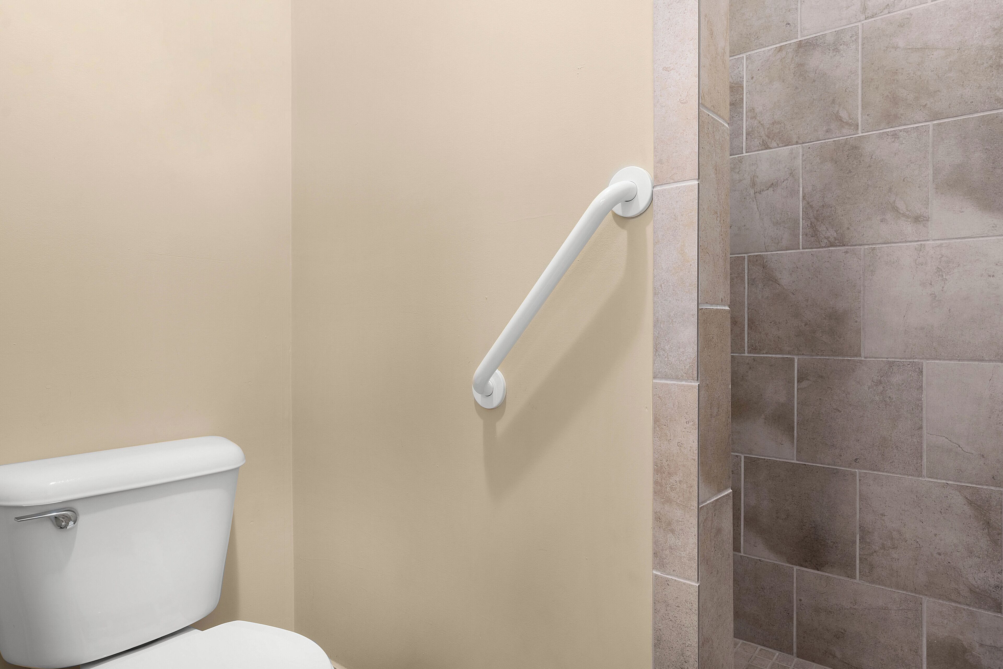 A bathroom with a beige wall, a white toilet, and a white grab bar.