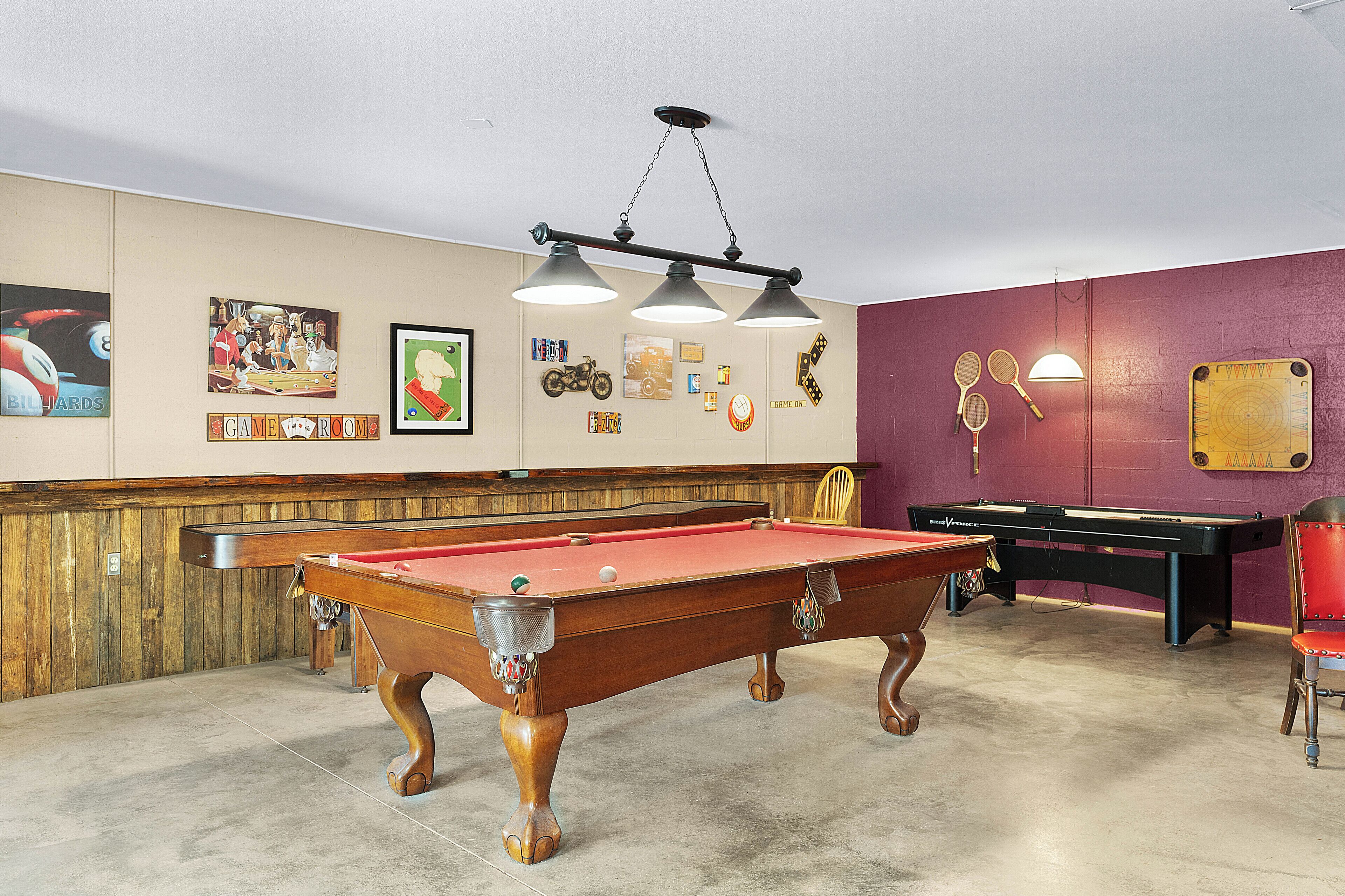 A pool table with a red felt surface, a billiards cue, and a pool table with a black felt surface.
