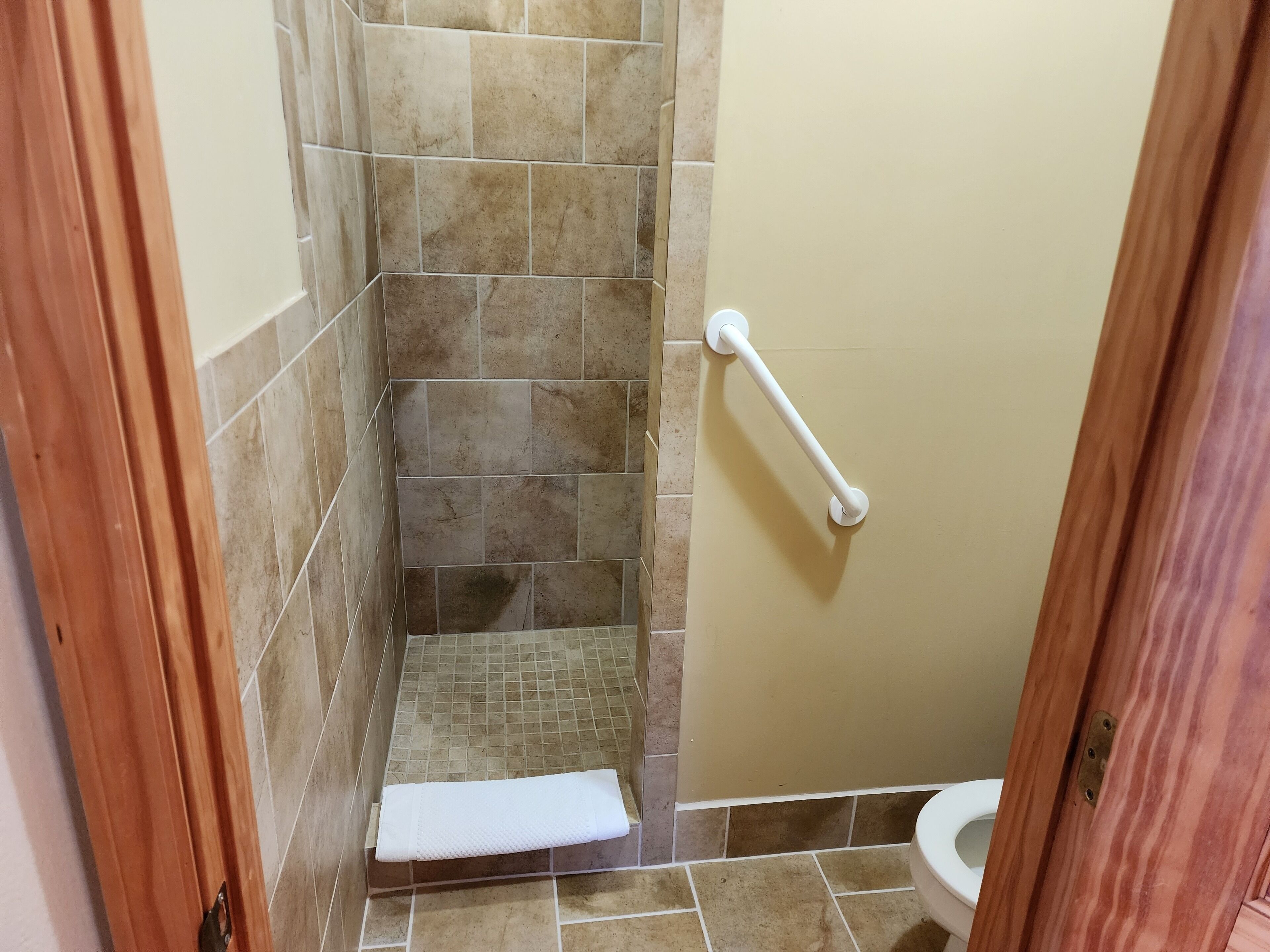 Un baño con zona de ducha, inodoro y una toalla blanca en el suelo.