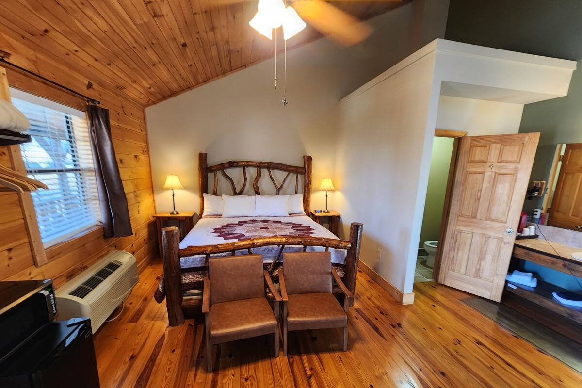 A cozy room with a wooden bed, two bedside lamps, a heater, and a small table with chairs.