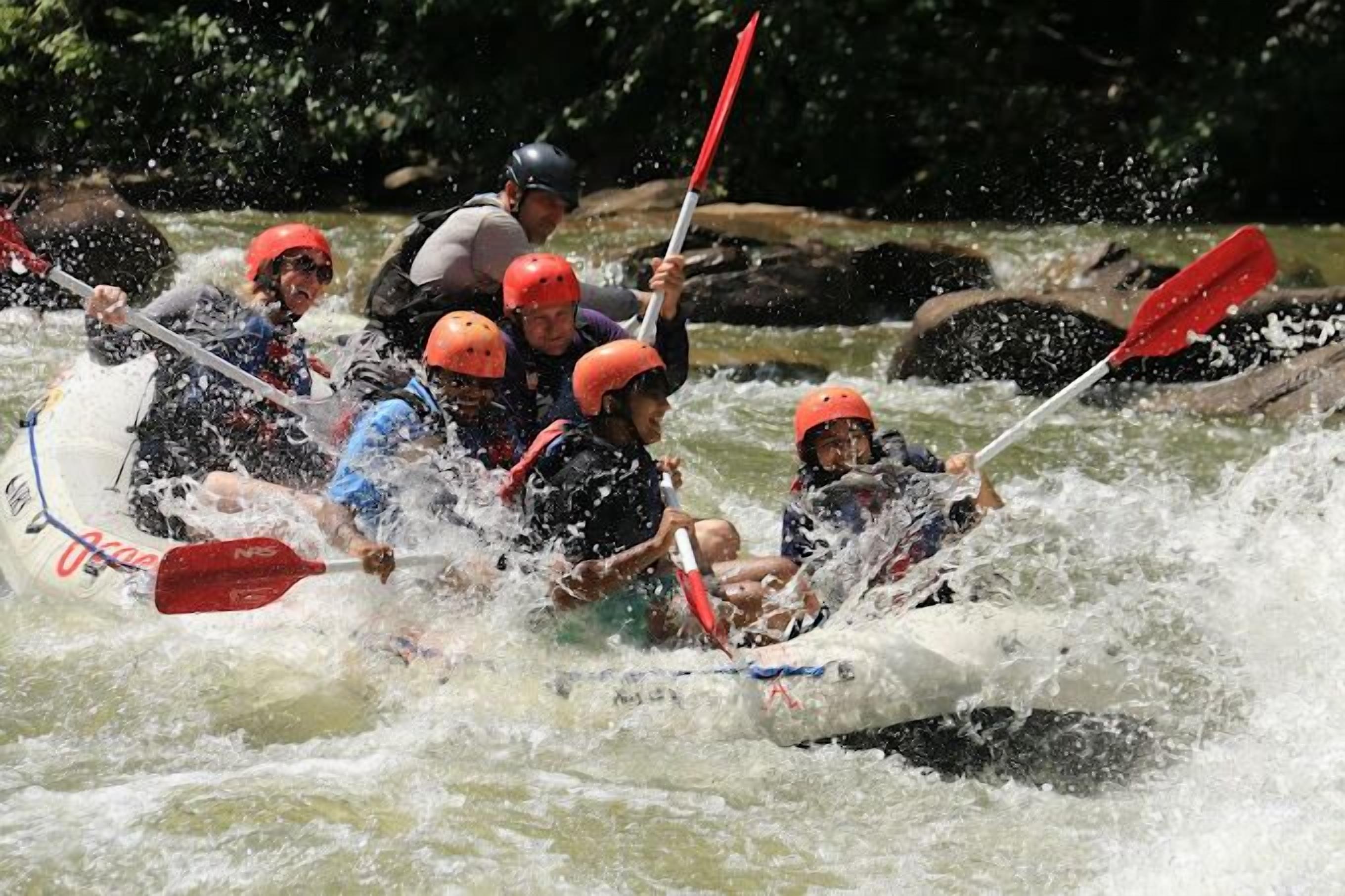 A group of people in a white raft with red paddles navigating through a river.