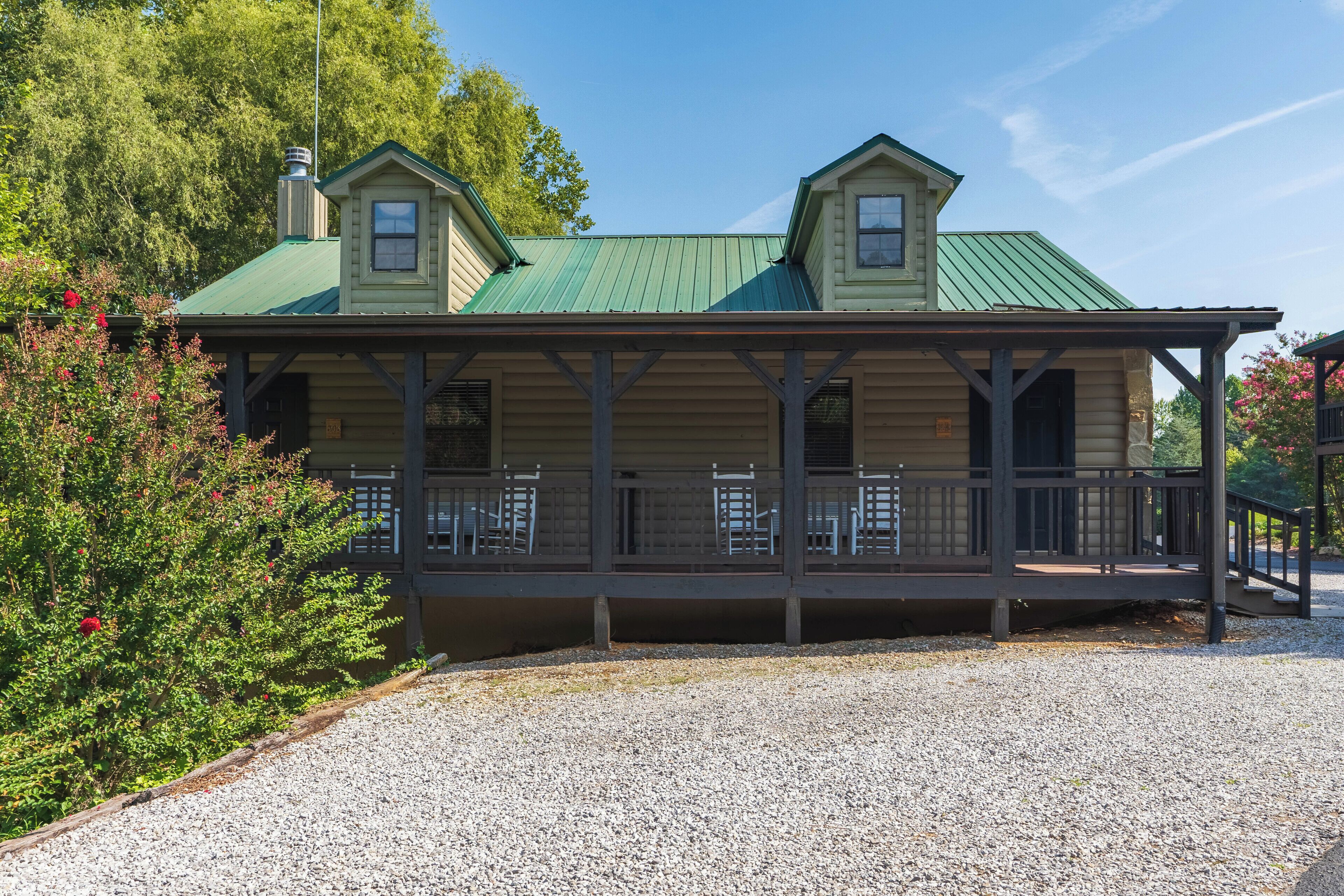A two-story building with a green roof and a covered porch with chairs.