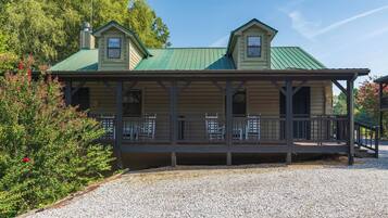 A two-story building with a green roof and a covered porch with chairs.