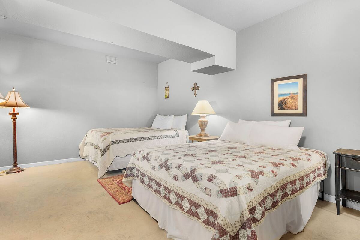 A bedroom with two beds, a nightstand, a lamp, a framed picture, and a small rug.