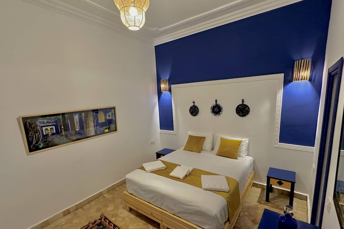 A bedroom with a large bed, a small table, a decorative rug, and wall art.