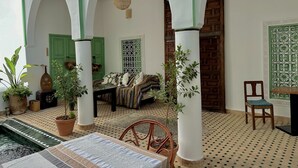 A traditional Moroccan interior with arches, a tiled floor, a sofa, a table, and potted plants. - Riad Ocallaghan (Marrakech)