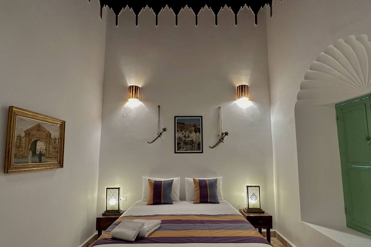 A bedroom with a bed, two wall-mounted lights, a framed picture, and a green door.