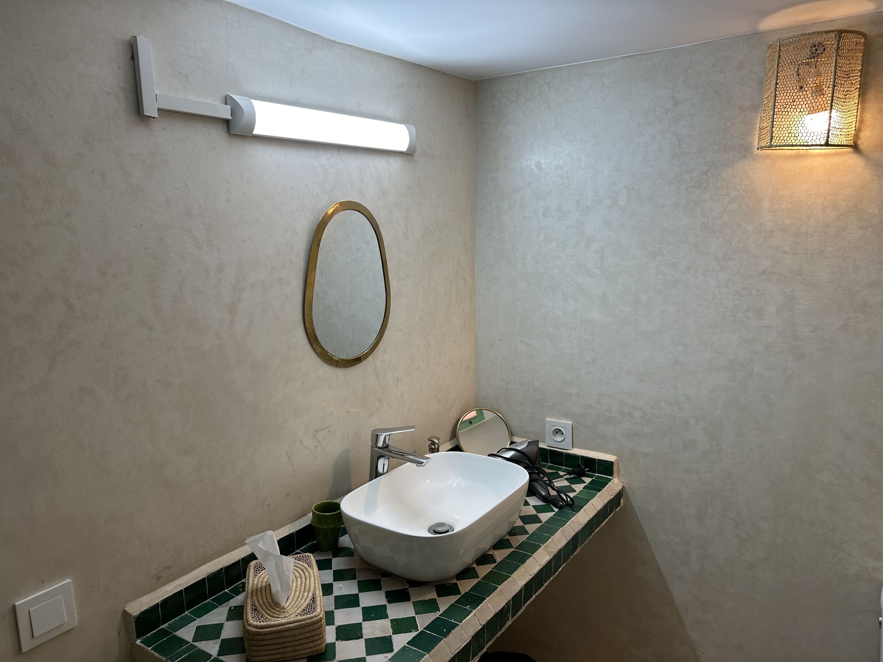 Un baño con lavamanos blanco, espejo, dispensador de toallas e iluminación en la pared.