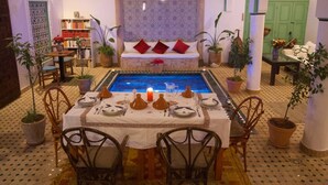 A dining area with a pool, potted plants, and a bookshelf. - Riad Ocallaghan (Marrakech)