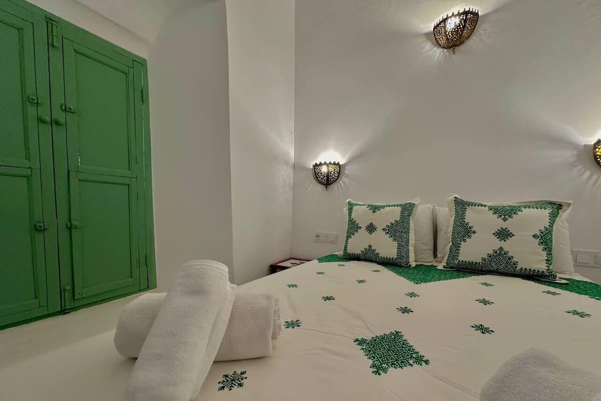 A bedroom with a bed, green wall sconces, and a green wardrobe.