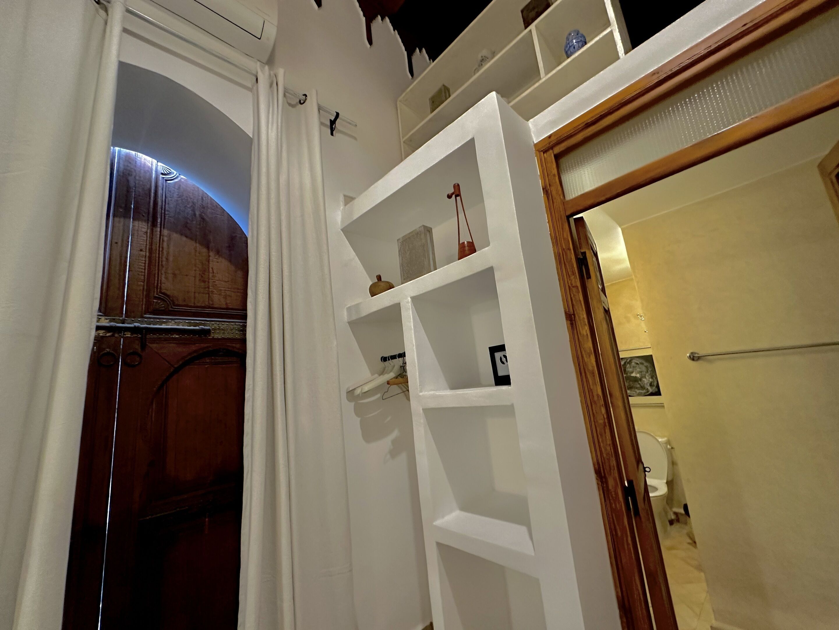 Une salle de bain avec un meuble en bois, une étagère blanche contenant divers objets et un espace douche.