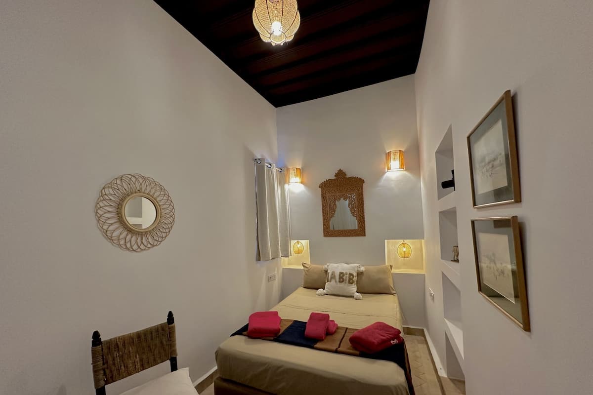 A bedroom with a bed, a chair, a mirror, and wall-mounted lights.