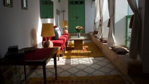 A cozy living room with a sofa set, a coffee table, and a lamp. There is a green door and a window with curtains. - Riad Ocallaghan (Marrakech)