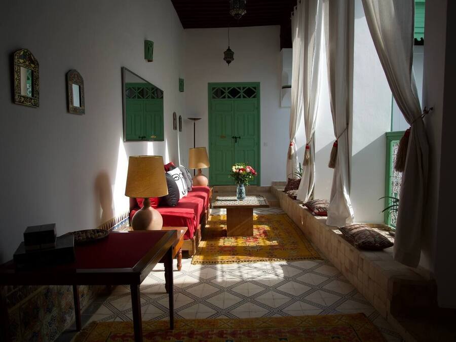 A cozy living room with a sofa set, a coffee table, and a lamp. There is a green door and a window with curtains.