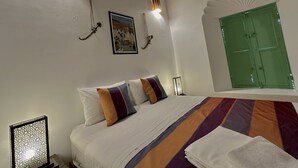 A bedroom with a bed, pillows, a wall-mounted picture, a green door, and a decorative fan. - Riad Ocallaghan (Marrakech)