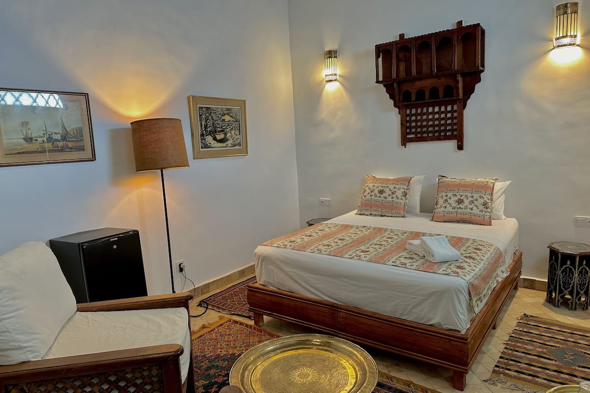 A bedroom with a wooden bed, a desk, a lamp, and a wall-mounted shelf.
