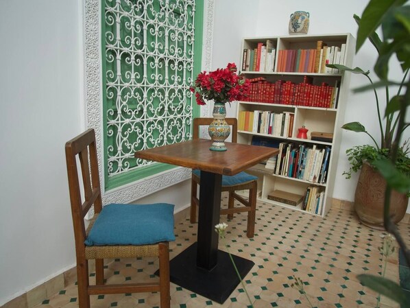 A room with a wooden table and chairs, a bookshelf, and a decorative window with a green patterned screen. - Riad Ocallaghan (Marrakech)