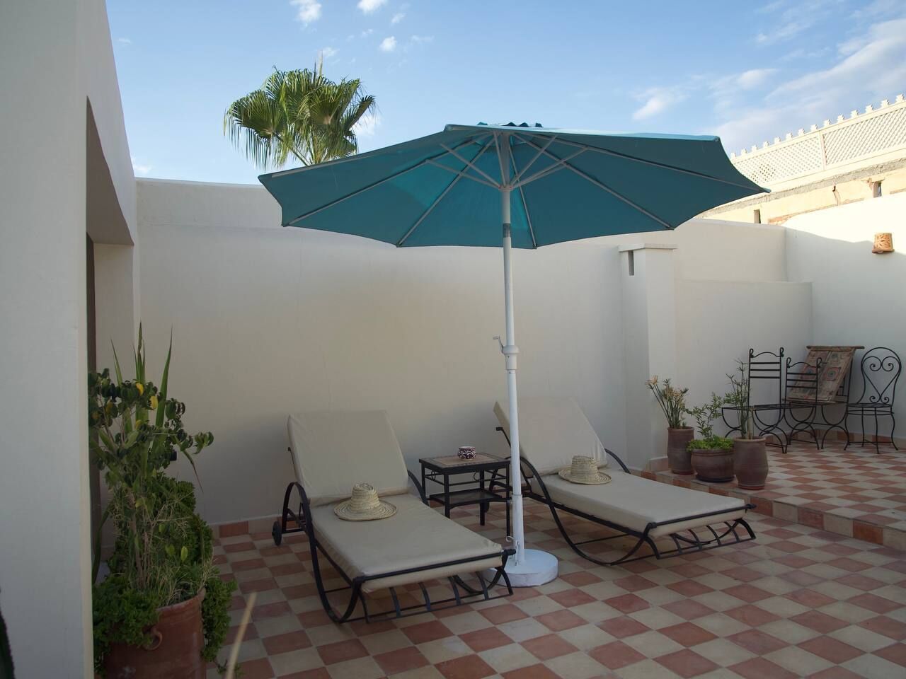 Eine sonnige Terrasse mit zwei Liegestühlen, einem türkisblauen Sonnenschirm und Topfpflanzen.