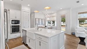A modern kitchen with white cabinetry, a central island, and a built-in oven. - 30A! Sleeps 8 • 2 Pools • Golf Cart • Pet Friendly (Inlet Beach)