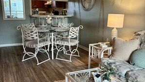 Un comedor con una mesa redonda y sillas blancas, una sala de estar con un sofá y una mesa de centro, un reloj de pared y una pequeña cocina.