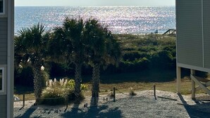 Vista de una playa con cielo despejado, palmeras y un edificio en primer plano.
