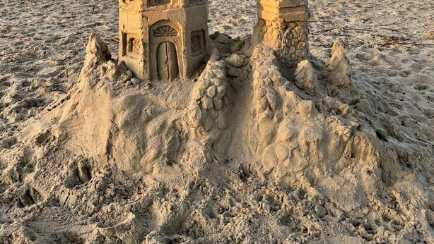 Un castillo de arena con una torre y una construcción más pequeña en la playa.