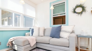 A corner living room with a grey sectional sofa, a small side table, and a window with blinds. - Dewey Beach House.  Just steps from the Ocean and all the Dewey fun spots (Dewey Beach)