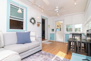 A modern living room with a grey sofa, a dining table with stools, and a ceiling fan. - Dewey Beach House.  Just steps from the Ocean and all the Dewey fun spots (Dewey Beach)