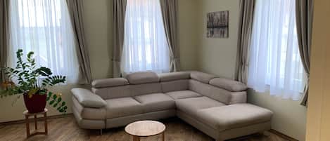 A living room with a sectional sofa, a small round table, and a potted plant.