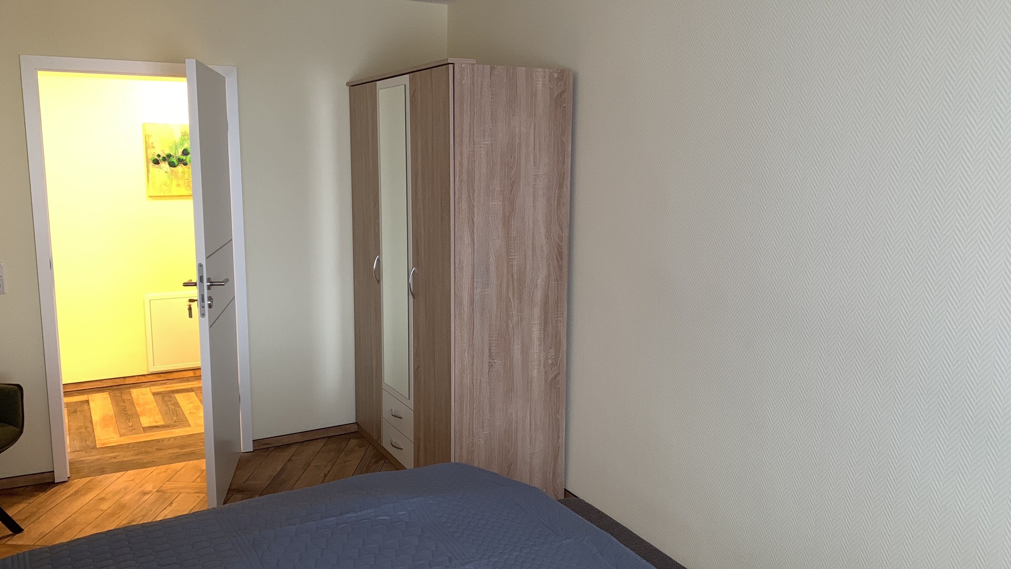 Een slaapkamer met een bed, een kledingkast en een deur naar een andere kamer.